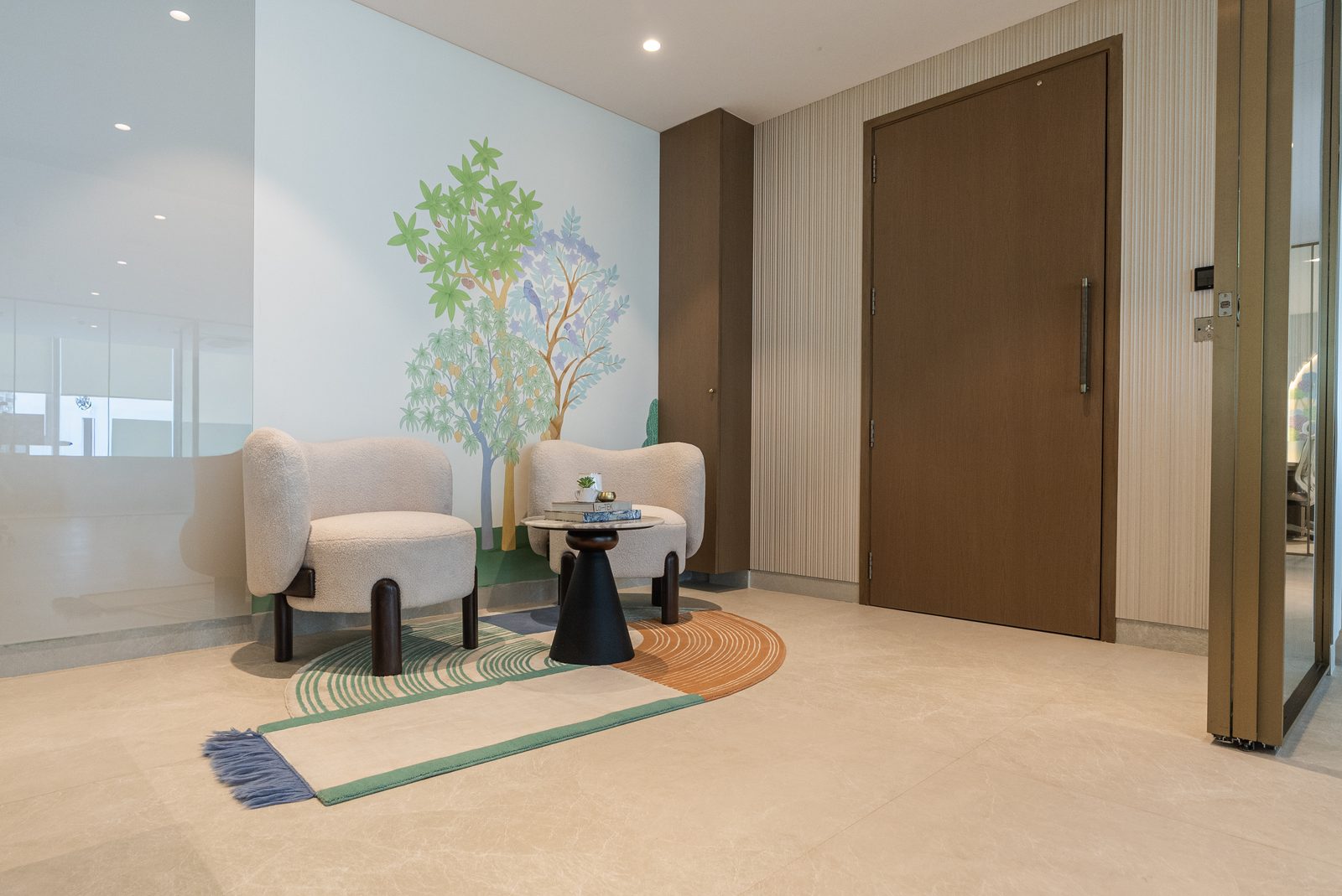 The entry corner with boucle chairs, a tree mural and a hand knotted rug